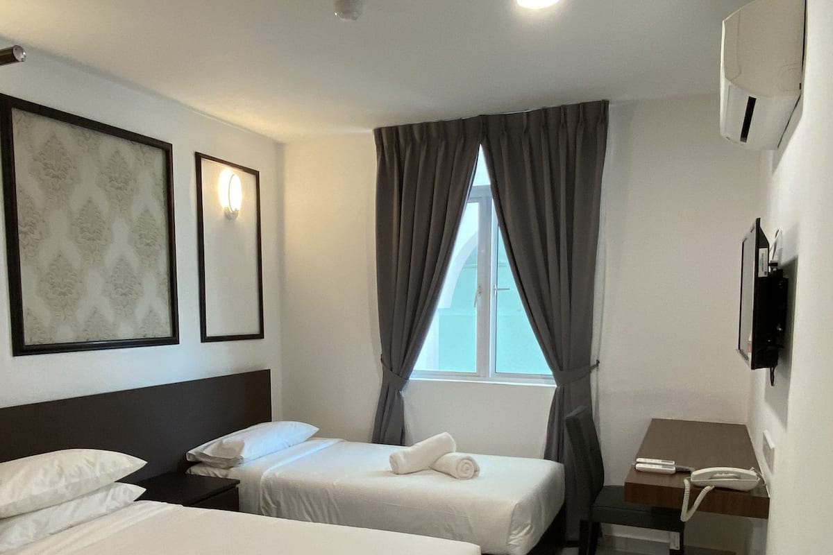 A hotel room with two beds, a desk, a chair, a phone, and a window with curtains.
