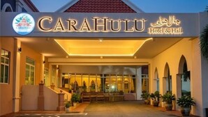 Entrada de hotel com placa indicando 'CARAHULU Hotel & Hall', uma galeria coberta e plantas em vasos ao longo das laterais.