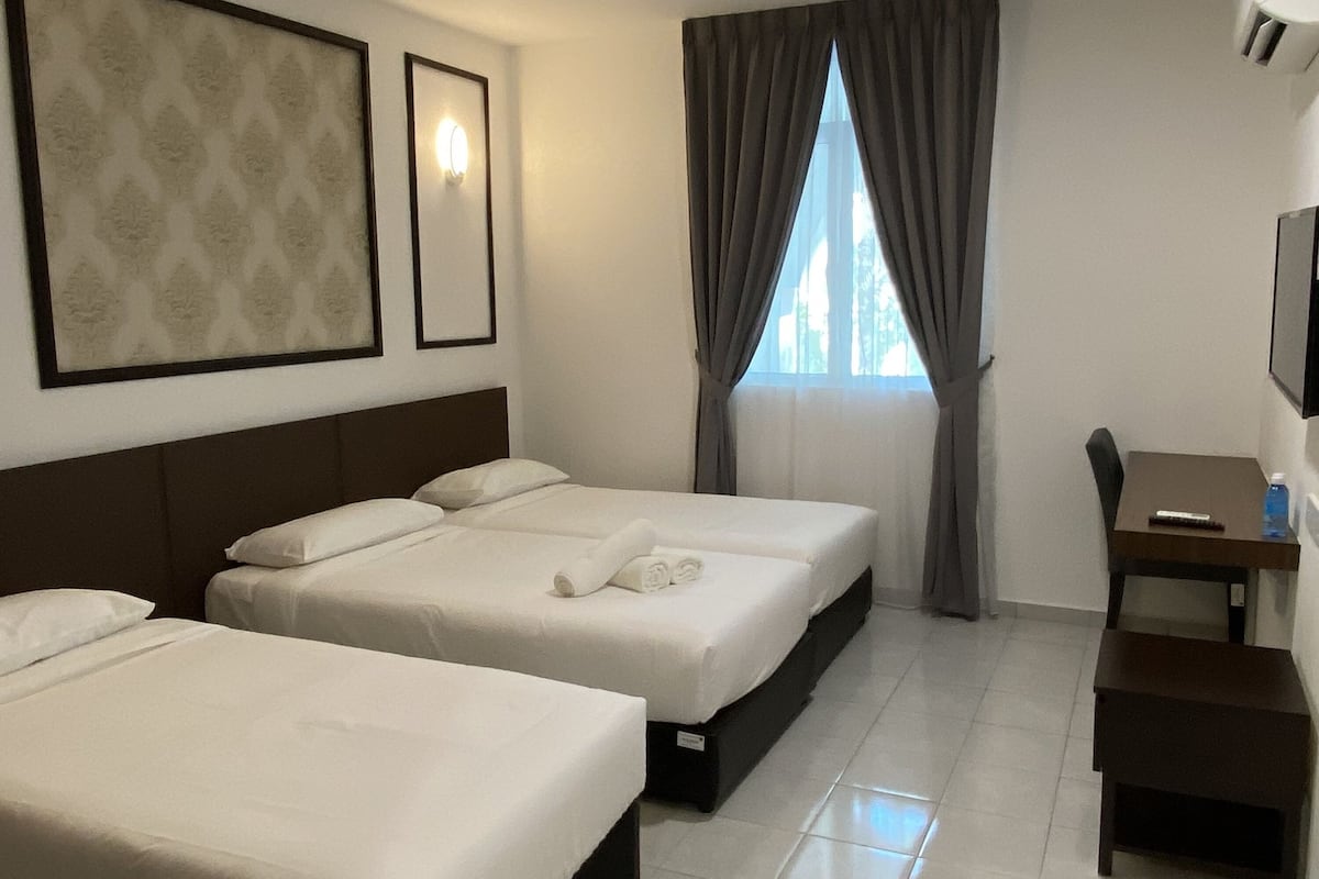 A hotel room with two beds, a desk, a chair, a TV, and a window with curtains.