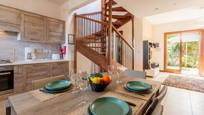 Une cuisine moderne avec des meubles en bois, un coin repas avec une table en bois dressée pour quatre personnes, et un escalier menant à l’étage supérieur.