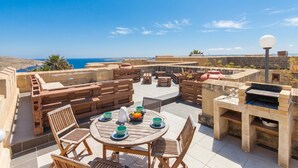 Une terrasse extérieure avec une table ronde, des chaises et un barbecue.