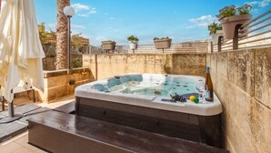 A hot tub with a stone wall backdrop, surrounded by potted plants and a white umbrella. - Harbour Views Gozitan Villa + Shared Pool, Mġarr Gozo, Malta (Mġarr Gozo)