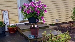 Ein Vorgarten mit einem Willkommensschild, einem Blumentopf mit violetten Blüten und einem Schild, auf dem steht: 