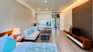 A modern hotel room with a bed, a sofa, a coffee table, a TV, a kitchen area, and a large window. - TASALA cabana (Tha Sala)