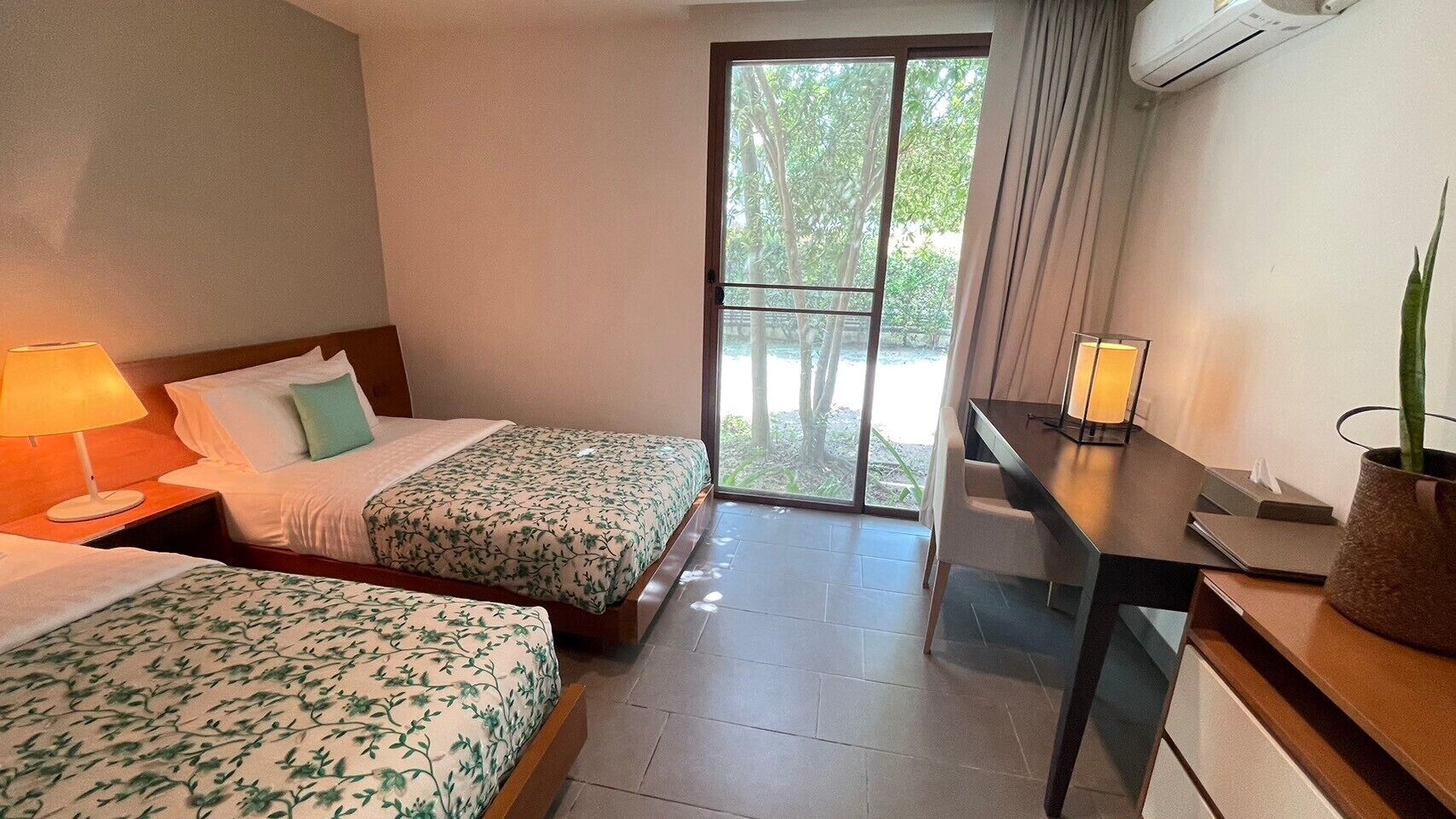 Una habitación de hotel con dos camas, un escritorio, una silla, una lámpara y una planta en maceta.