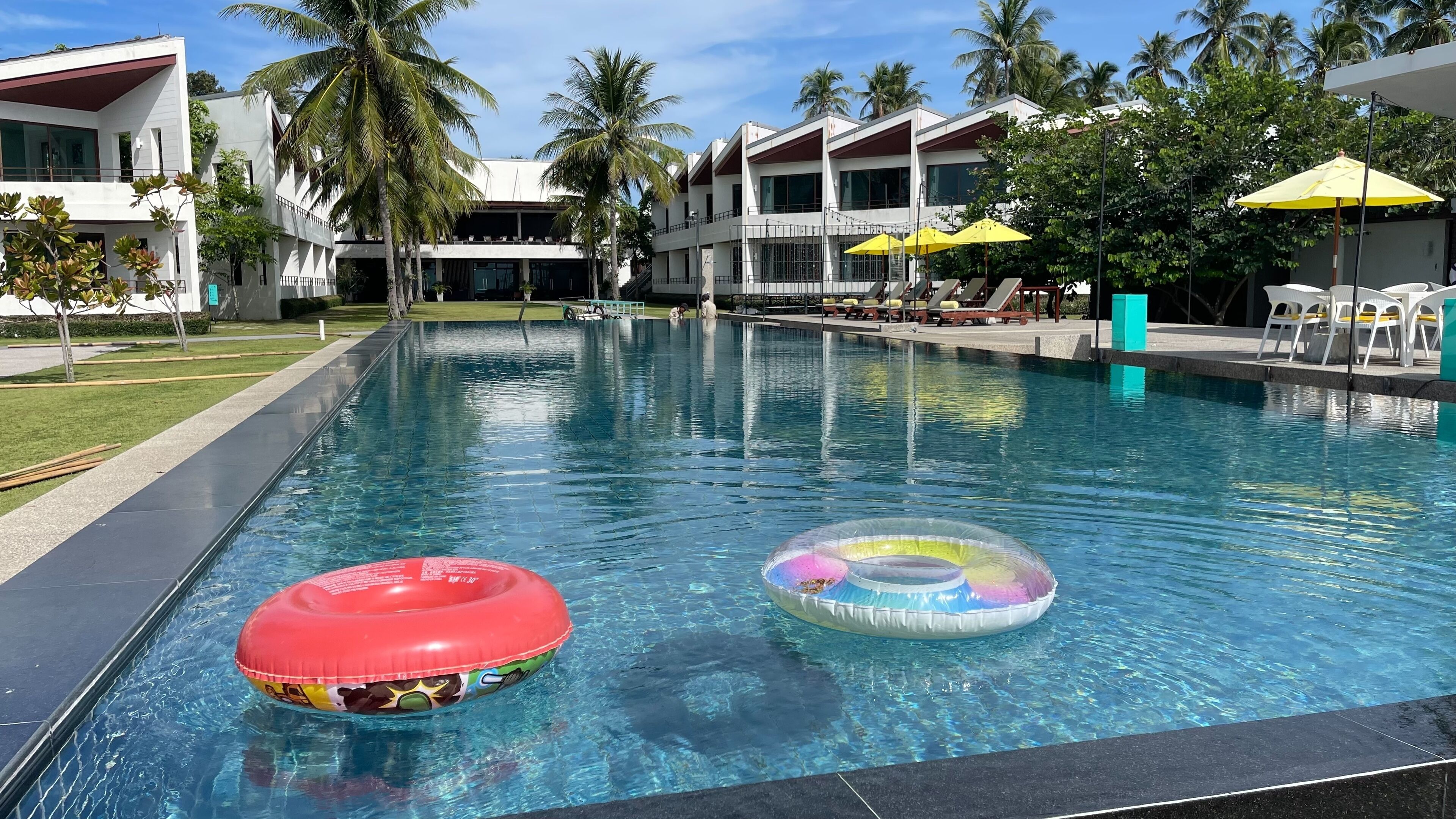 Una piscina con dos flotadores, rodeada de palmeras y un edificio con varios balcones.