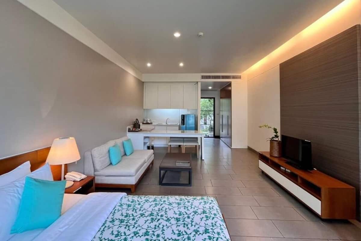 A hotel room with a bed, a sofa, a TV, a desk, and a kitchenette.