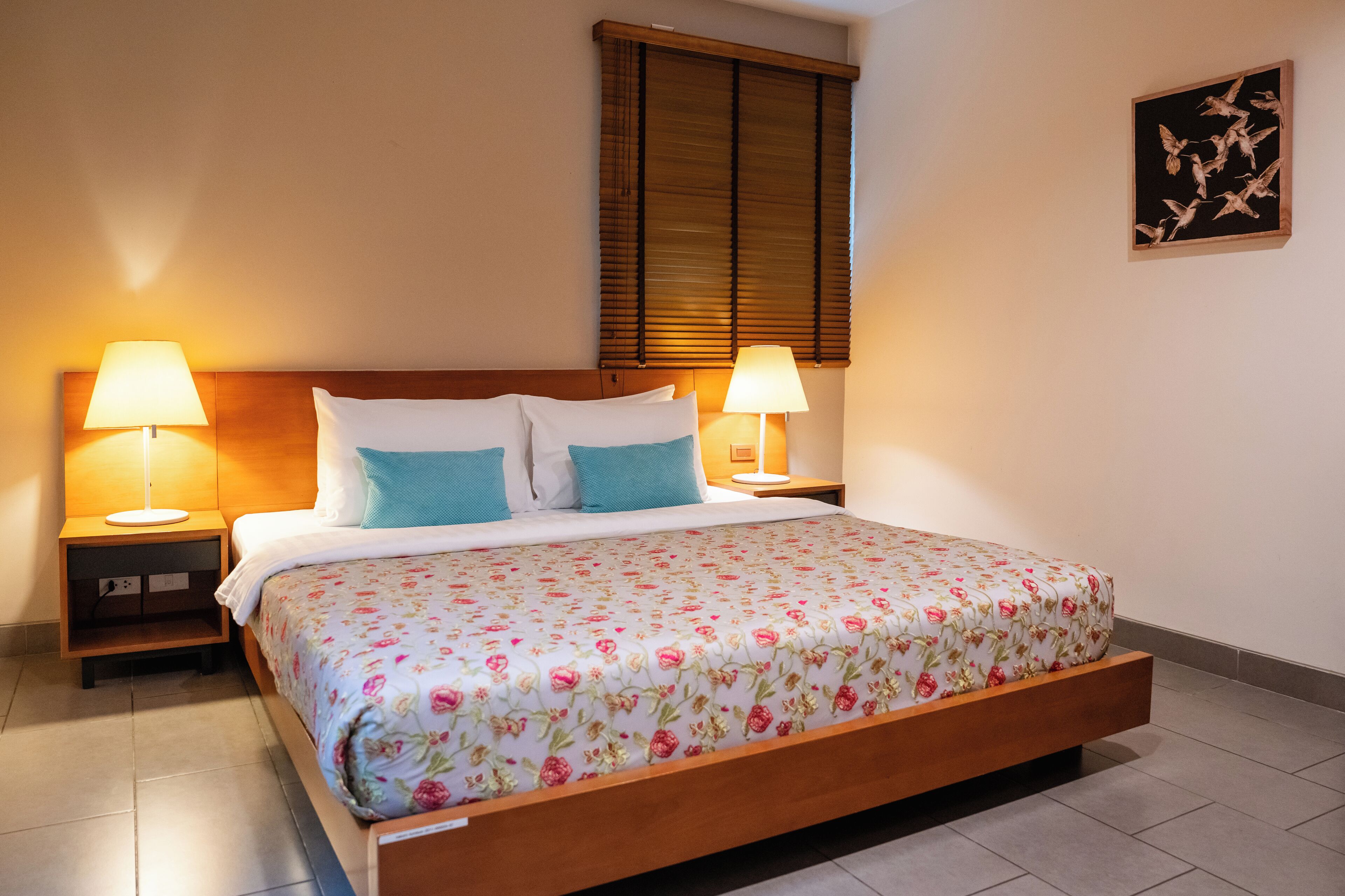 A neatly made bed with floral bedding, two bedside lamps, and a wooden headboard.