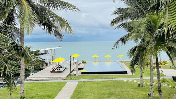 A pool area with lounge chairs and umbrellas, surrounded by palm trees and a view of the sea. - TASALA cabana (Tha Sala)