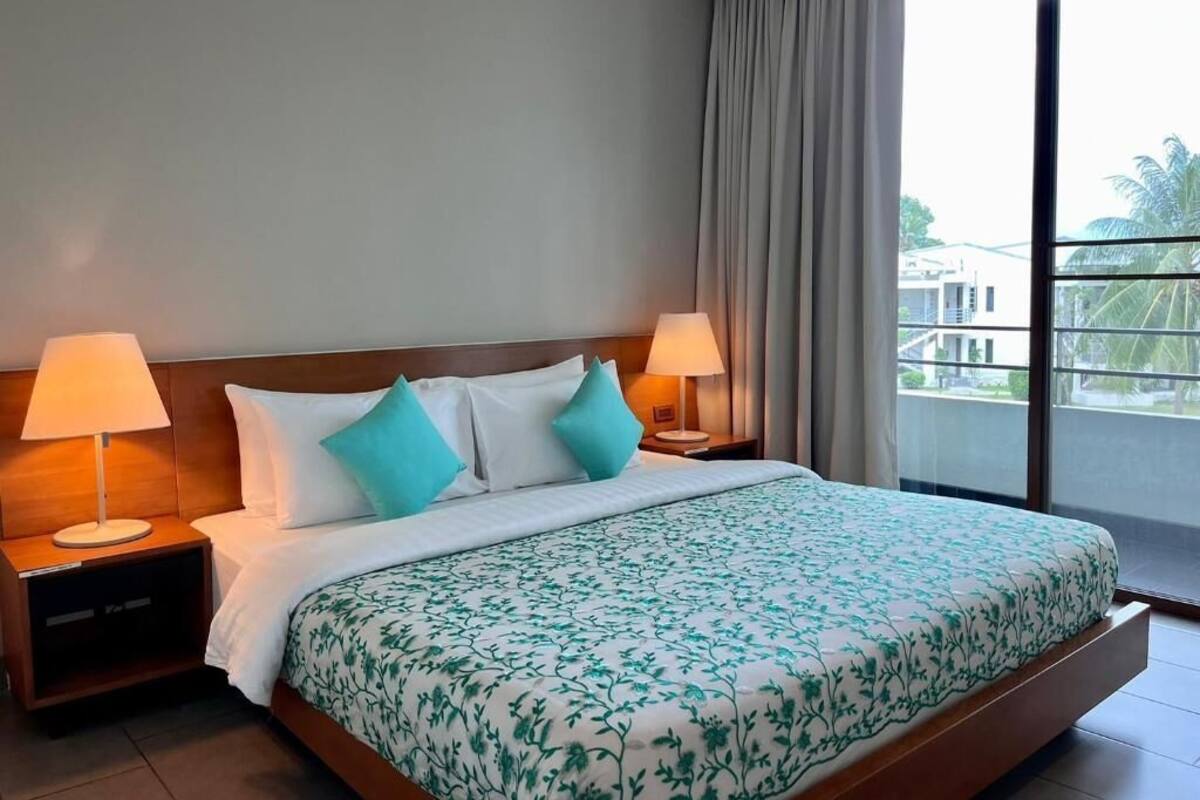 A hotel room with a large bed, two bedside lamps, a view of the outside, and a balcony.