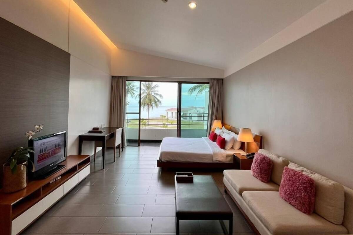 A hotel room with a bed, a sofa, a TV, a desk, and a balcony with a view.
