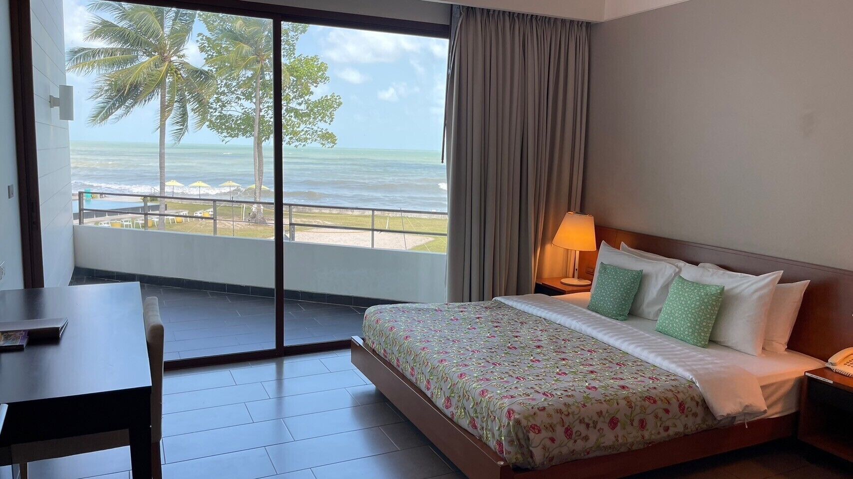 Una camera d'hotel con un letto, una scrivania e vista sull'oceano attraverso una grande finestra.
