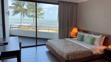 A hotel room with a bed, a desk, and a view of the ocean through a large window.