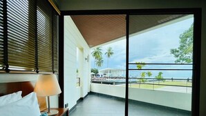 A hotel room with a large sliding glass door leading to a balcony with a view of the sea and palm trees. - TASALA cabana (Tha Sala)