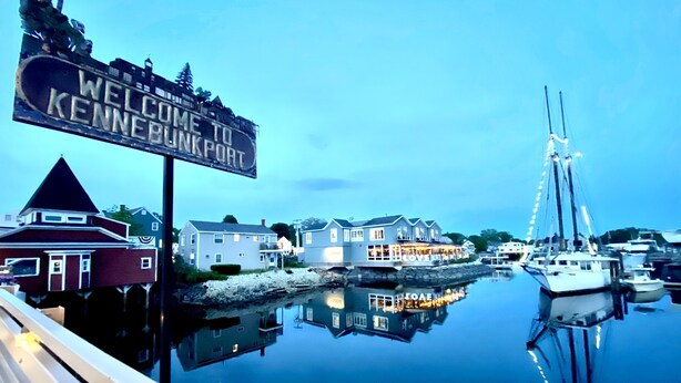 Une vue sur le front de mer, avec une pancarte indiquant « Bienvenue à Kennebunkport », une rangée de maisons et un voilier amarré au quai.