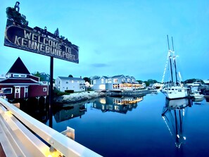 A waterfront view with a sign reading "Welcome to Kennebunkport," a row of houses, and a sailboat docked at the pier. - Beautiful, Oceanfront Home, Perfect Location near Downtown KPT! (Kennebunk)