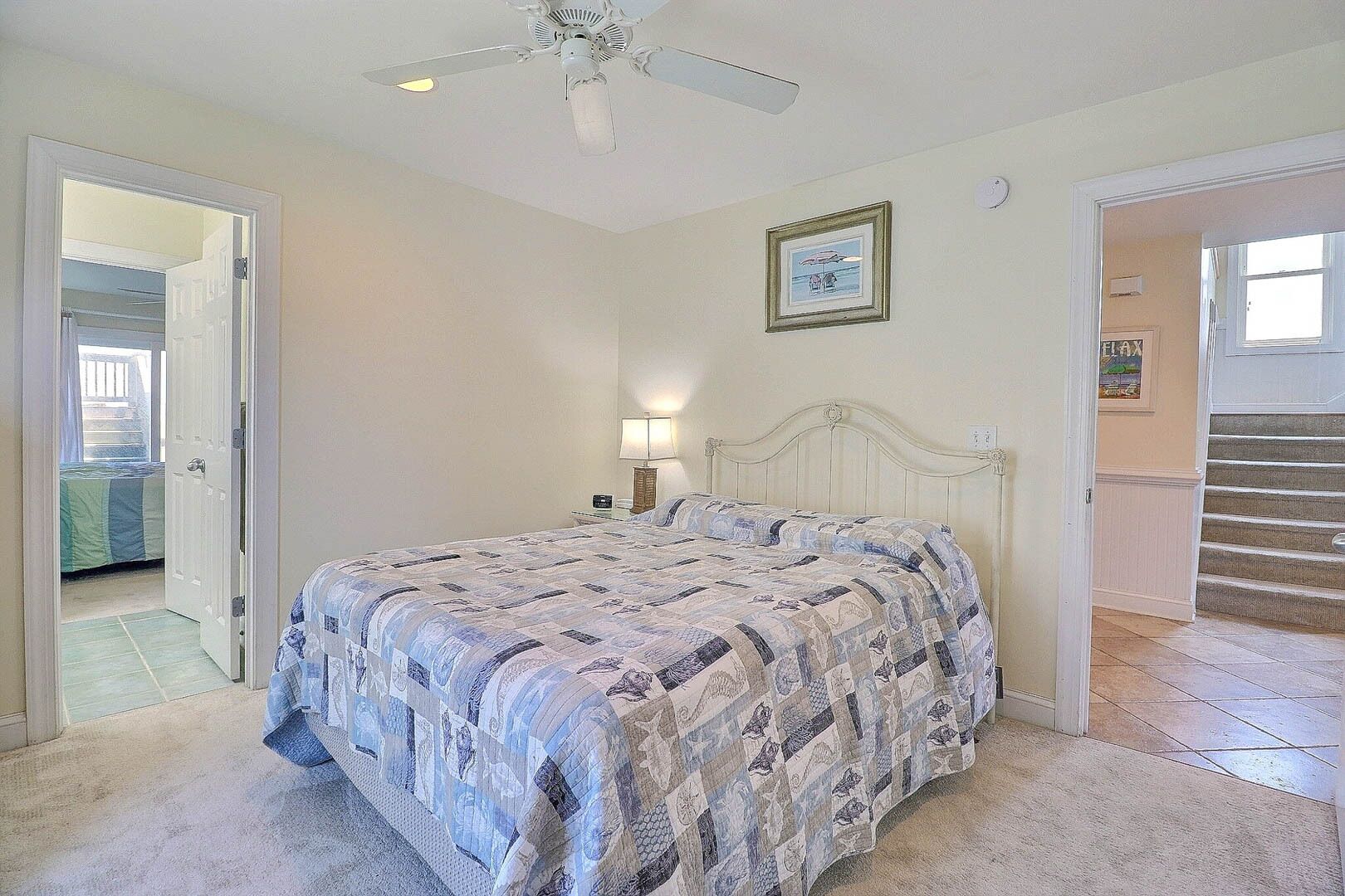 A bedroom with a bed, a ceiling fan, a nightstand, a lamp, and a framed picture on the wall.