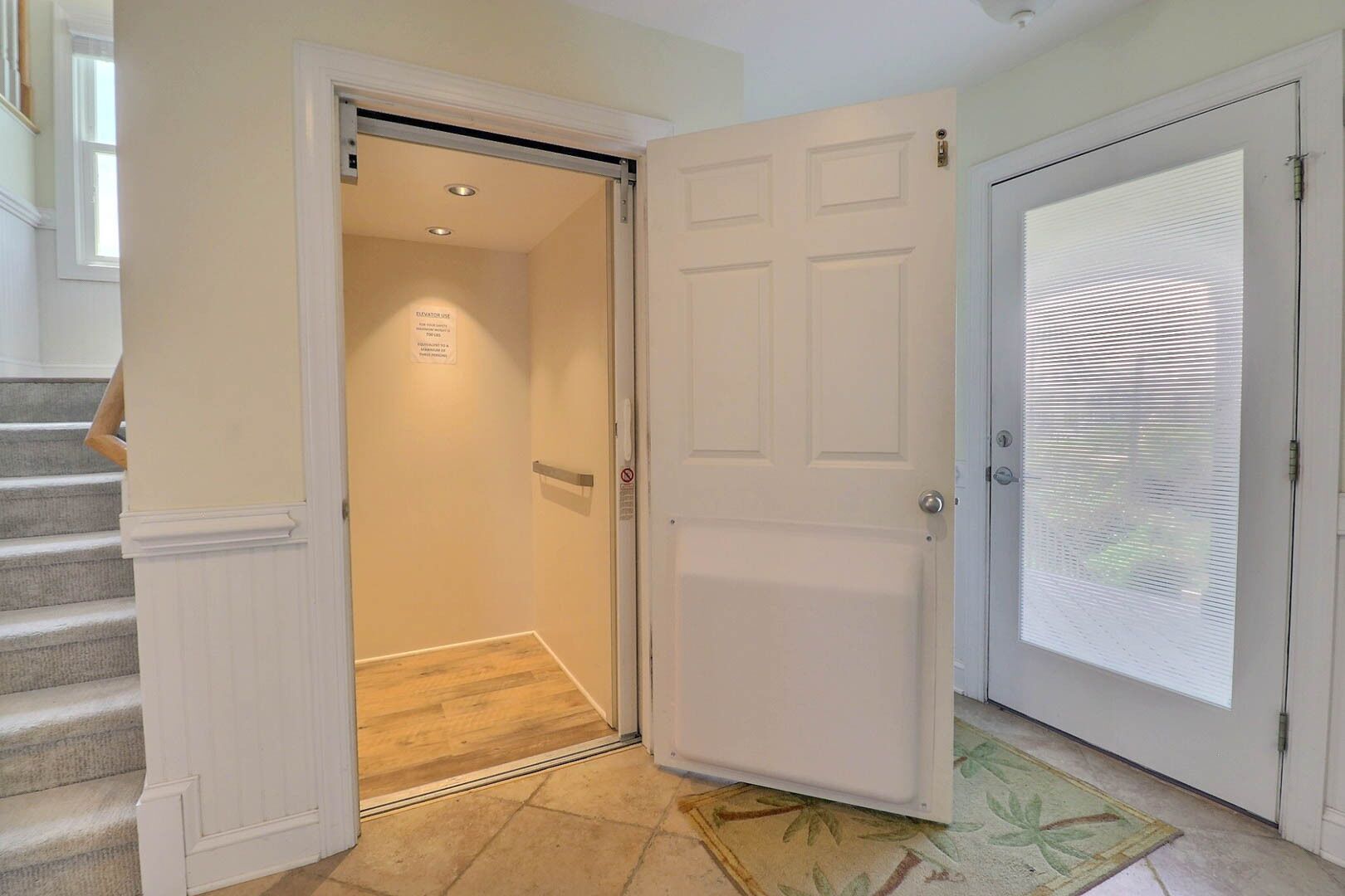 Un pasillo con una puerta que da a una habitación, una escalera y un ventanal con persianas.