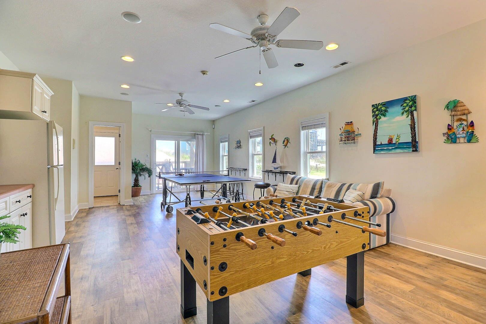 A spacious living room with a foosball table, ceiling fans, and a large window providing natural light.