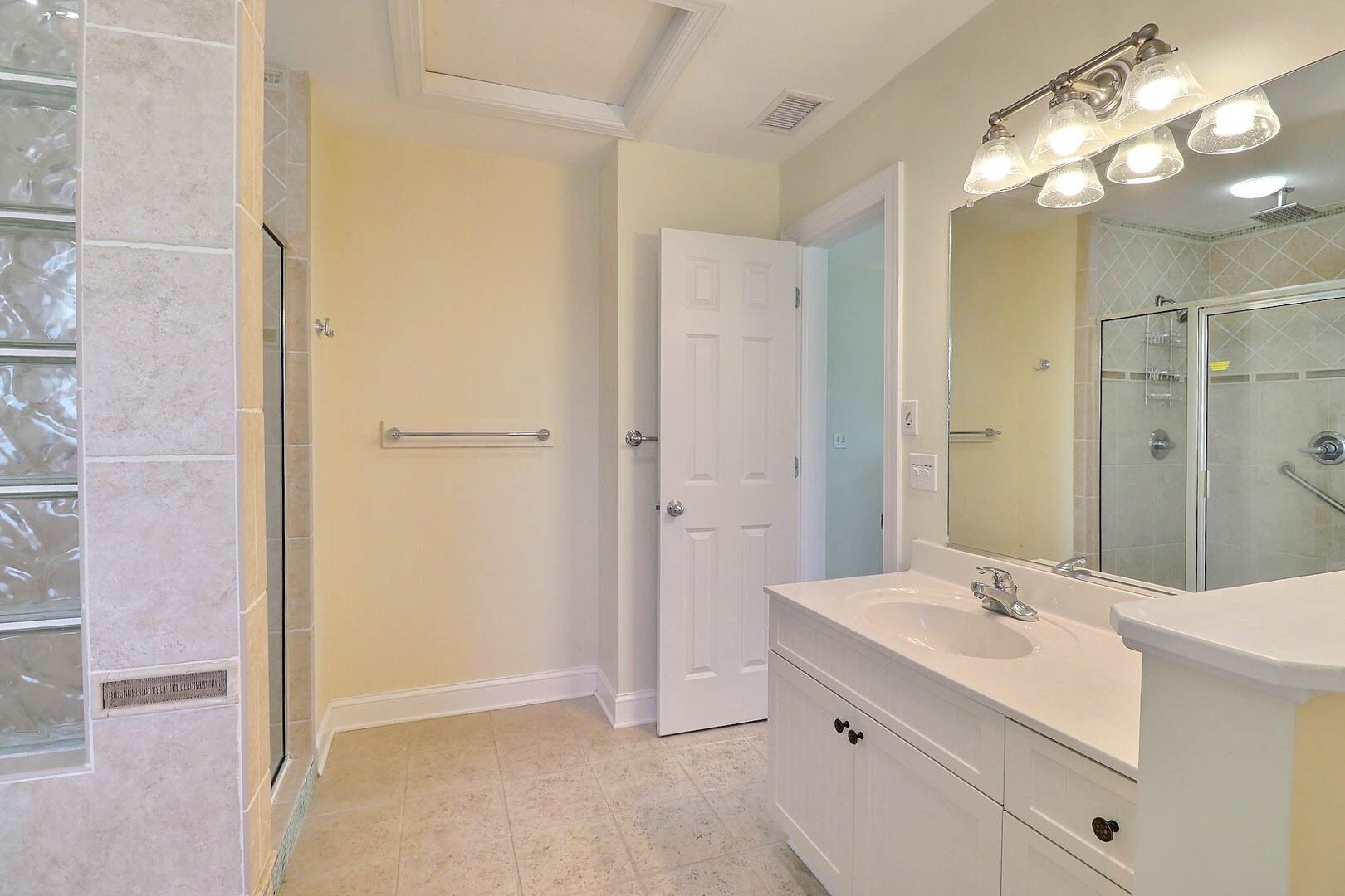 A bathroom with a shower, a vanity with a sink, and a mirror.