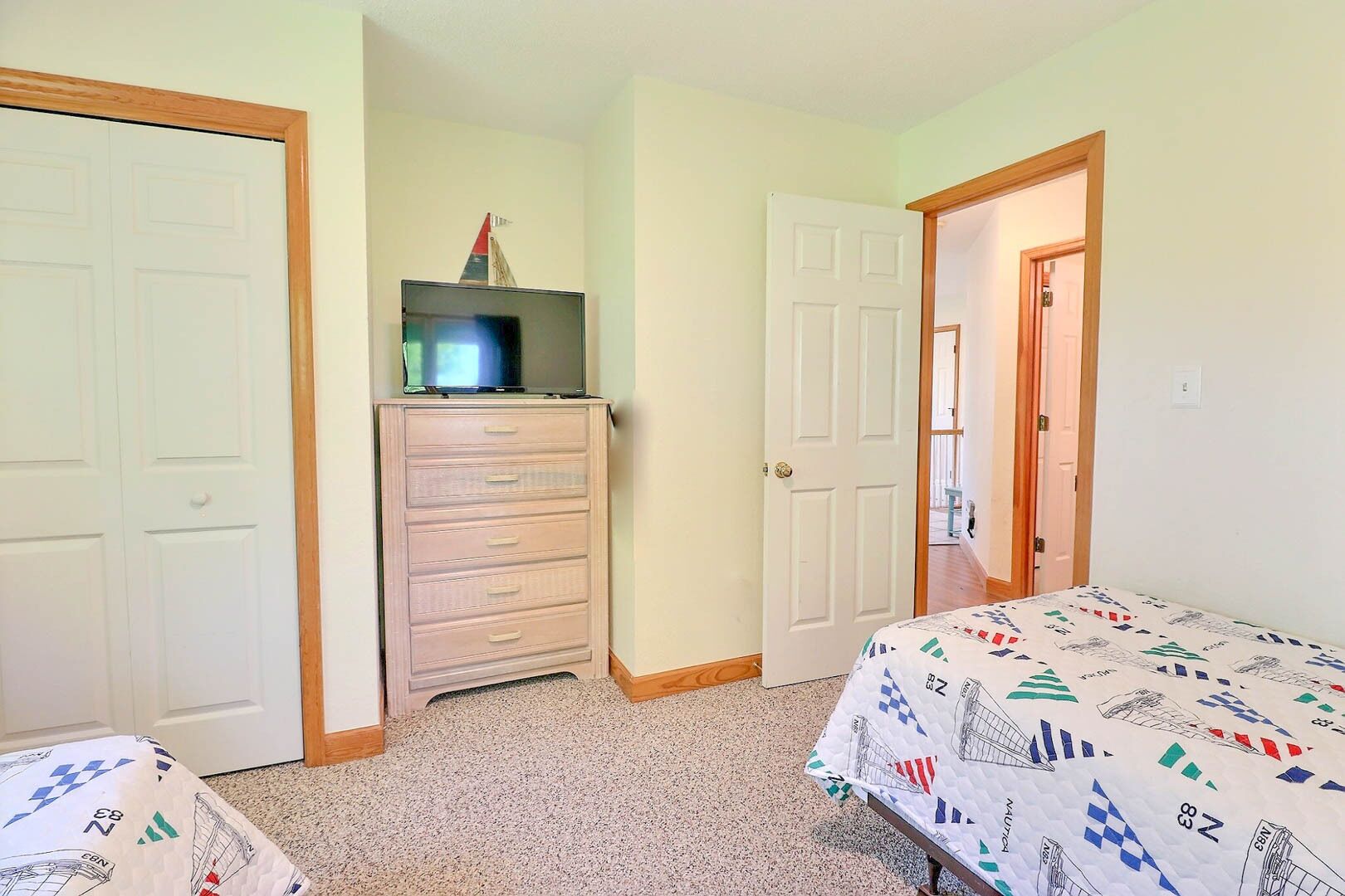 A bedroom with a bed, dresser, television, and two doors.