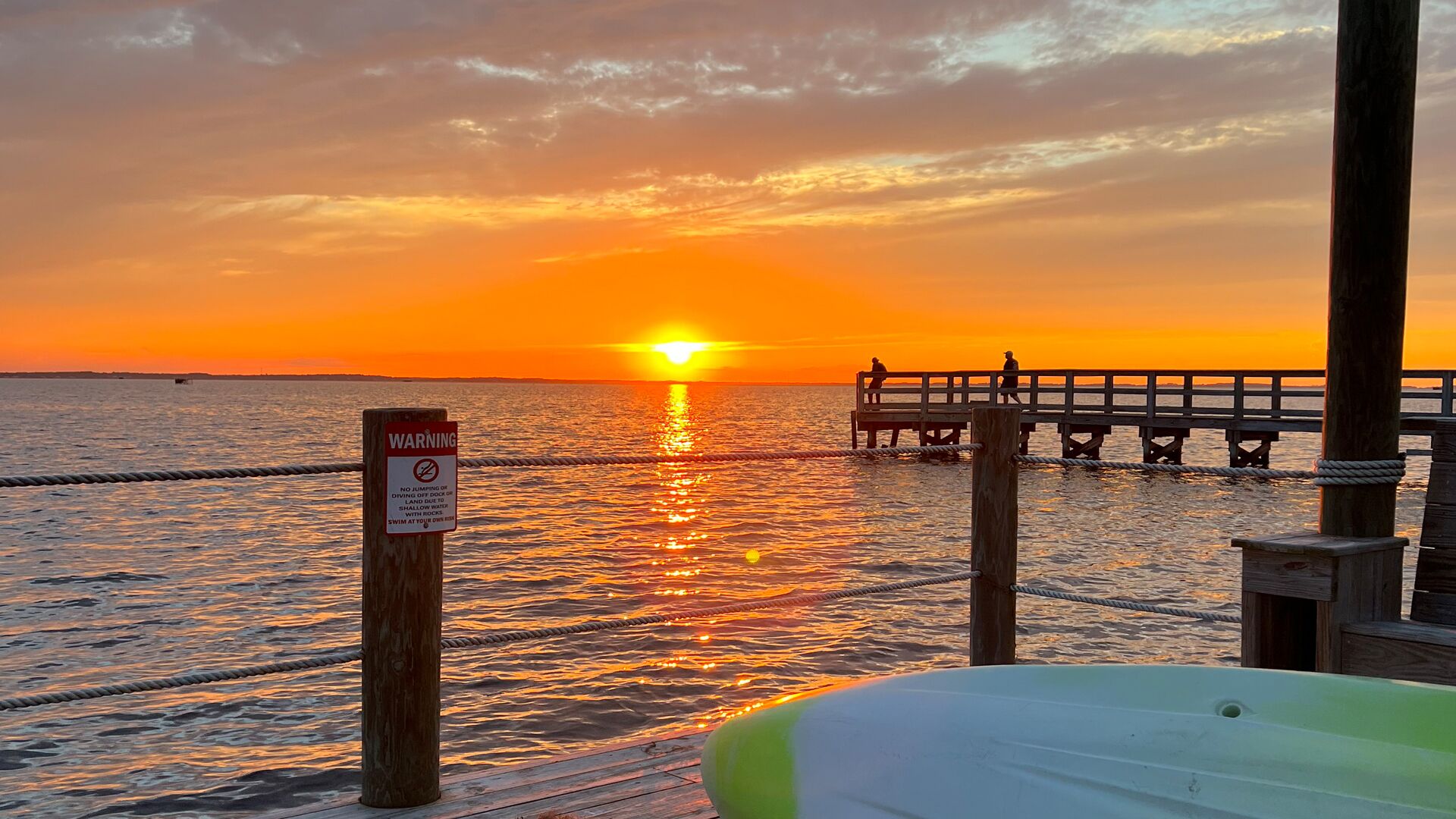 A sunset over water with a wooden pier and a warning sign.