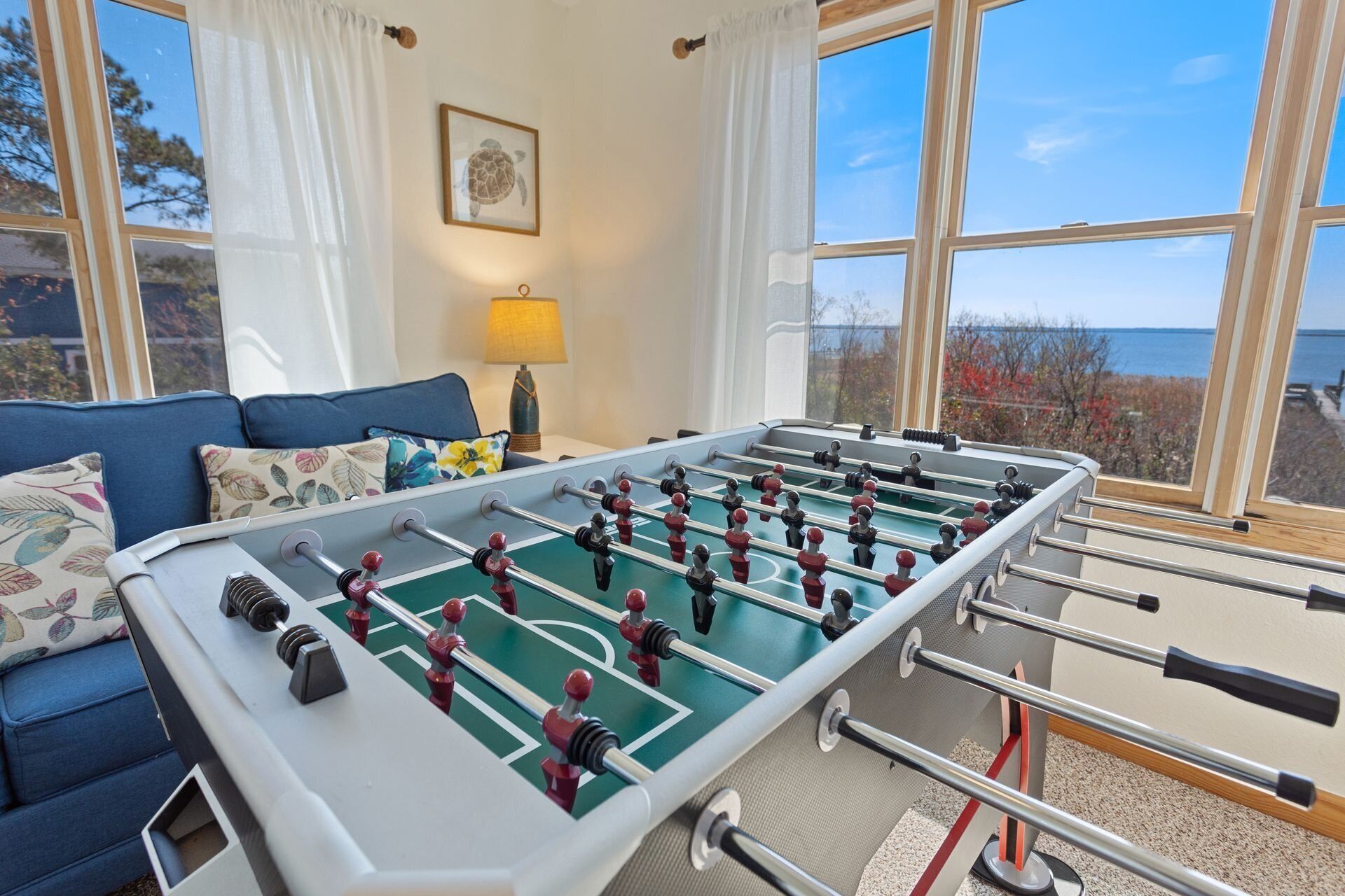 Een tafelvoetbaltafel in een kamer met uitzicht op zee, een blauwe bank en een lamp.