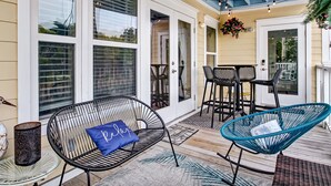 A covered patio with outdoor seating, including a chair with a 'Relax' pillow, a table, and a hanging chair. - Heated Pool | 5*Clean | Flex Cancelation (Tybee Island)