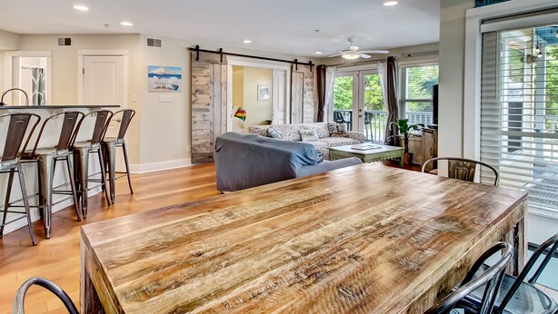 A spacious living area with a wooden dining table, a sofa, and a ceiling fan. - Heated Pool | 5*Clean | Flex Cancelation (Tybee Island)