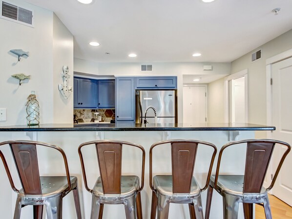 A modern kitchen with blue cabinets, stainless steel appliances, and a central island with bar stools.