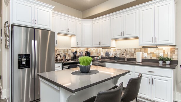 A modern kitchen with white cabinetry, a stainless steel refrigerator, a central island with chairs, and a tiled backsplash.