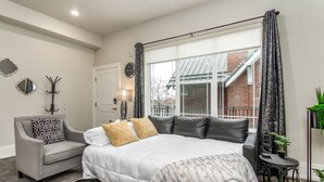 A bedroom with a large bed, a grey armchair, a small side table, and a window with curtains.