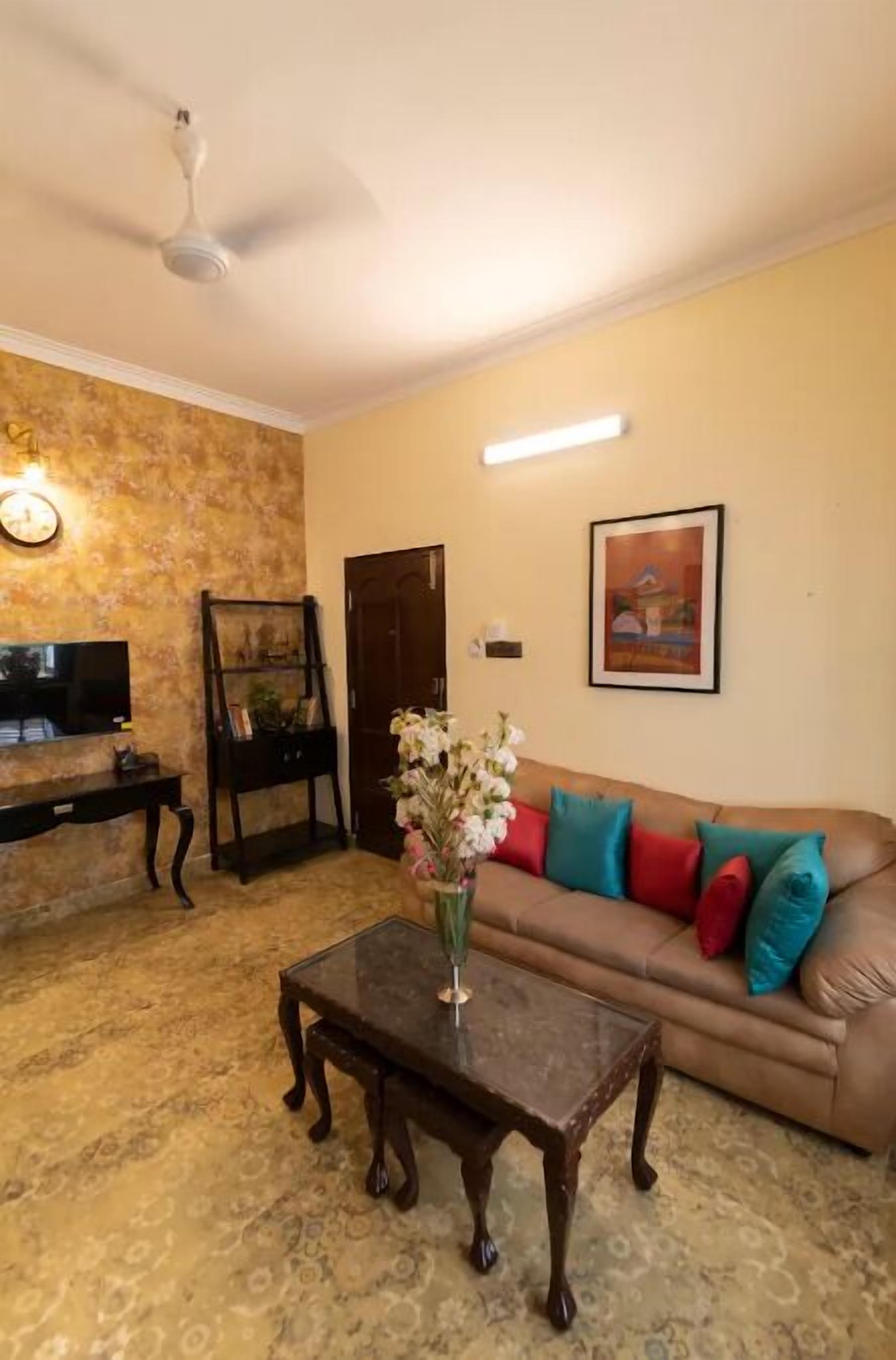 Un salon avec un canapé marron, une table basse en bois, un téléviseur, un ventilateur de plafond et un tableau accroché au mur.