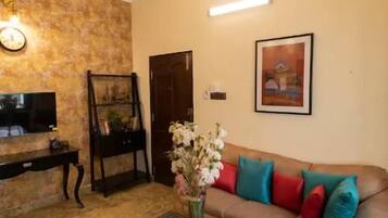 Un salon avec un canapé marron, une table basse en bois, un téléviseur, un ventilateur de plafond et un tableau accroché au mur.