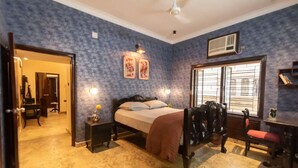 Quarto com cama, mesas de cabeceira, uma cadeira, escrivaninha e janela com persianas.