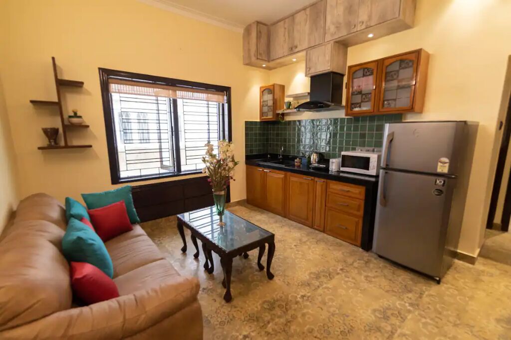 A compact living space with a sofa, a coffee table, a kitchen area including a refrigerator, microwave, and wooden cabinets.