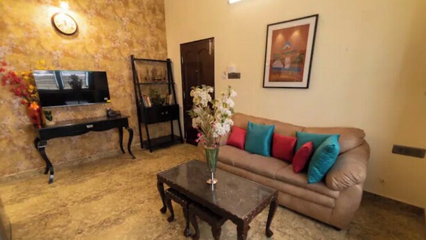 Uma sala de estar com sofá, mesa de centro, TV em um móvel, quadro na parede e um vaso com flores.