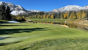 Een golfbaan met een vijver, bomen en bergen op de achtergrond.