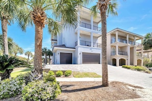 A multi-story residential building with a white facade, multiple balconies, and a driveway leading to a garage.