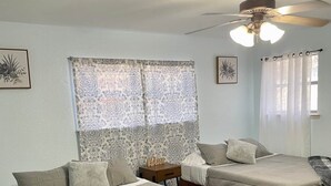 A bedroom with two beds, a ceiling fan, patterned curtains, and a wooden nightstand.
