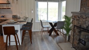 Une cuisine dotée d’un grand îlot central, de chaises en bois, d’une table à manger avec des chaises, d’une cheminée en pierre et d’une grande fenêtre offrant une vue dégagée.