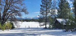 Paisaje nevado con una cabaña de madera y una vista despejada de montañas distantes.
