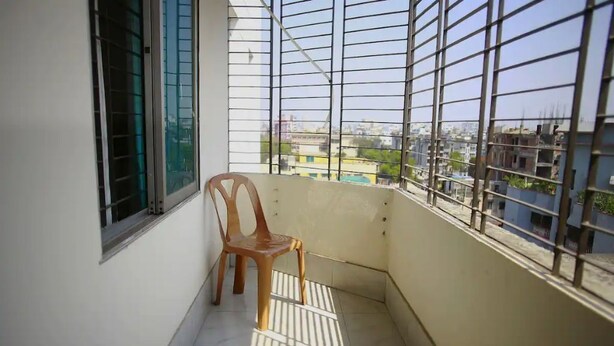 A balcony with a view of the cityscape, a window with metal bars, and a plastic chair. - 💗AC,ATTACH BATH ROOM,NEAR LALMATIA MOHAMADPUR (Dhaka)