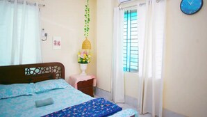 A bedroom with a bed, a bedside table with a lamp, a window with curtains, and an air conditioning unit. - 💗AC,ATTACH BATH ROOM,NEAR LALMATIA MOHAMADPUR (Dhaka)