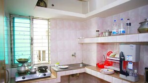 A kitchen with a gas stove, sink, and window with bars. There are shelves with kitchenware and bottles. - 💗AC,ATTACH BATH ROOM,NEAR LALMATIA MOHAMADPUR (Dhaka)