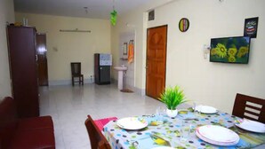 Zona de dinar amb una taula preparàda per a quatre, un frigorífic, un rentaplat i una porta que condueix a una altra habitació.