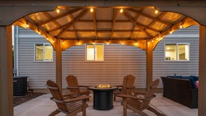 An outdoor patio with wooden chairs, a fire pit, and string lights under a wooden pergola. - Unrivaled Location, Hot Tub, Huge Patio w/ Gazebo and Couches, Pool Table, Ping Pong, Walk to Dundee (Dundee)