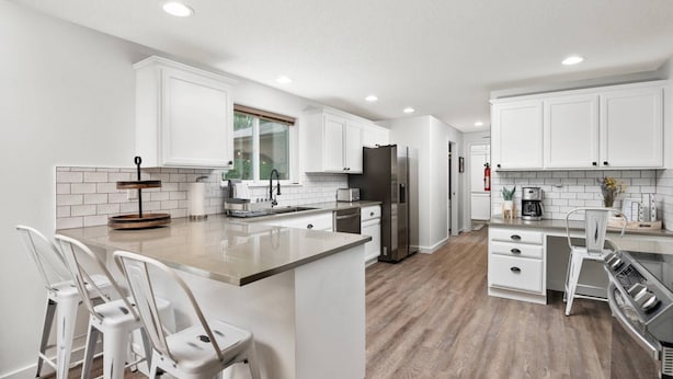 A modern kitchen with white cabinetry, a central island with bar stools, a stainless steel refrigerator, and a built-in oven. - Unrivaled Location, Hot Tub, Huge Patio w/ Gazebo and Couches, Pool Table, Ping Pong, Walk to Dundee (Dundee)