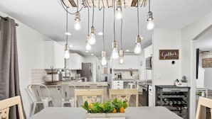 A modern kitchen with white cabinets, a dining area with a wooden table and chairs, and a wine rack. - Unrivaled Location, Hot Tub, Huge Patio w/ Gazebo and Couches, Pool Table, Ping Pong, Walk to Dundee (Dundee)