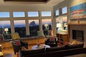 A living room with a view of a mountain at dusk, large windows, a fireplace, and modern furnishings.